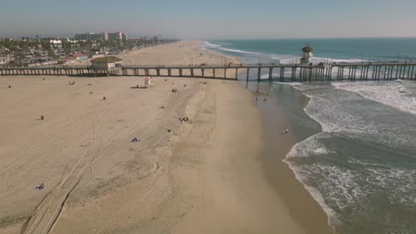 Erleben-Sie-Die-Schönheit-Des-Huntington-Pacific-Pier-Boardwalk-Mit-Diesem-Faszinierenden-Drohnen-Zeitraffer,-Der-Die-Wellen-Und-Das-Küstenleben-An-Sonnigen-Tagen-Zeigt
