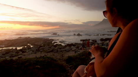 Mother-with-pet-dog-watching-over-kids-playing-on-coastline-at-sunset