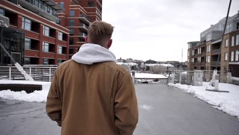 slo-mo-walk-and-pan-around-a-blonde-young-man-with-brown-a-brown-jacket-on-Millennium-Bridge-in-Denver-Colorado-on-cold-snowy-day