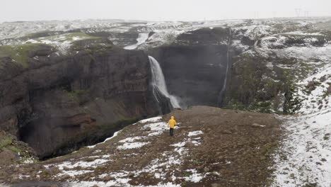 Aerial:-One-man-walking-near-the-edge-of-a-cliff-towards-Granni-waterfall-in-Iceland