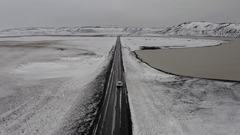 Aerial:-Following-a-car-driving-on-a-snowy-road-near-a-frozen-lake