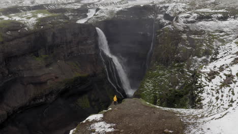 Aerial:-Flyover-one-person-wearing-yellow-jacket,-looking-at-Granni-waterfall-in-Iceland