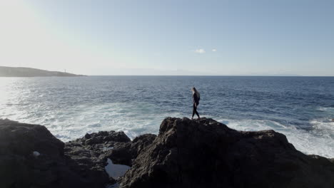 aerial-shot-on-young-woman-walking-on-rock-near-the-sea-and-surf
