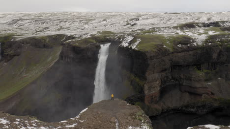 Aerial:-One-person-wearing-yellow-jacket,-looking-at-Haifoss-waterfall
