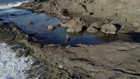 Aerial-shot-with-tracking-of-a-young-woman-who-walks-between-the-natural-pools-and-where-the-waves-of-the-sea-can-be-appreciated