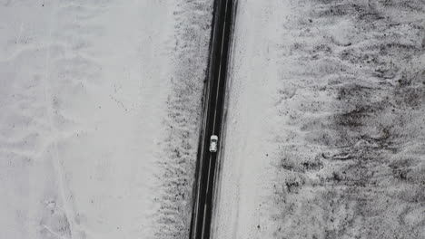 Aerial:-Top-down-follow-shot-of-one-car-driving-on-a-snowy-road-in-Iceland