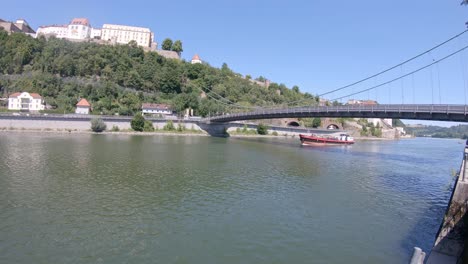 Barcaza-Navega-En-El-Río-Danubio,-Fortaleza-Histórica-De-Passau-En-El-Paisaje-De-La-Colina-Y-El-Puente