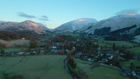 Flying-over-English-village-at-dawn-towards-sunrise-lit-snowy-mountains-at-Grasmere