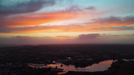 Luftdrohnenaufnahme-Eines-Dunstigen-Sonnenuntergangs-über-Der-Stadt-Galway-Mit-Einer-Wunderschönen-Himmelsreflexion-Auf-Dem-Fluss