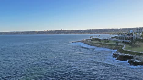 Panning-drone-shot-showing-horizonline-and-trail-with-ocean-waves-crashing-on-cliffs-in-La-Jolla,-California-during-King-Tide