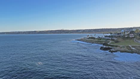 Panning-drone-shot-with-horizonline-and-trail-with-waves-crashing-on-cliffs-in-La-Jolla,-California-during-King-Tide