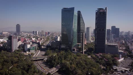 Group-of-skyscrapers-on-Paseo-de-la-Reforma-Avenue-in-Mexico-City-taken-with-a-drone-on-a-sunny-and-clear-day,-next-to-it-is-a-large-avenue-with-several-cars-circulating