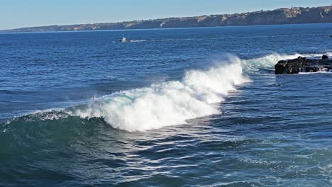 Drone-shot-of-waves-crashing-on-reef-while-sea-lions-play-and-pelican-flys-by-with-boat-in-background-in-La-Jolla-California-during-king-tide
