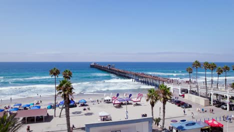 Drone-Rising-Over-Oceanside-Pier-with-Many-People-at-Beach-in-Summer