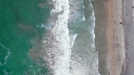 Top-Down-View-of-Beach-Waves-Washing-on-Shore-Near-Oceanside-Pier-with-Swimmers-in-Water