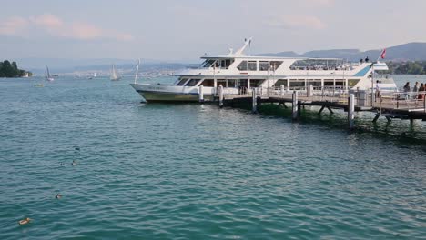 Passengers-boarding-ferry-moored-to-pier-of-harbour-by-Lake-Zurich-before-cruise