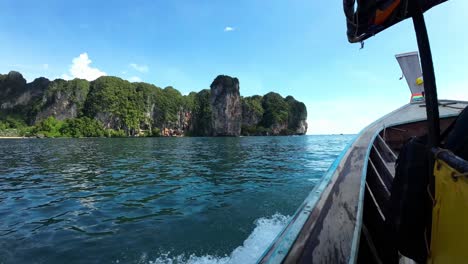 Long-tail-boat-in-Railay,-Krabi,-Ao-Nang,-South-Thailand-on-the-ocean-with-a-rocky-and-green-coastline-in-the-background