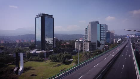 Shot-of-the-elevated-four-lane-peripheral-road-in-the-south-of-Mexico-City,-in-the-background-you-can-see-some-corporate-buildings-or-hotels,-the-day-looks-lightly-cloudy-and-sunny