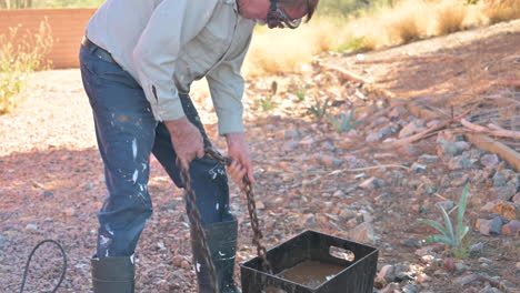 Male-worker-cleans-metal-chain-in-bucket-with-water-outdoors,-zoom-in