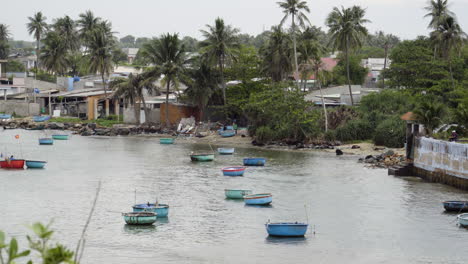 Fischerdorf-In-Vietnam-Mit-Einer-Reihe-Von-Schönen-Runden-Booten,-Die-Im-Wasser-Segeln,-Mit-Blick-Auf-Das-Dorf-Im-Hintergrund