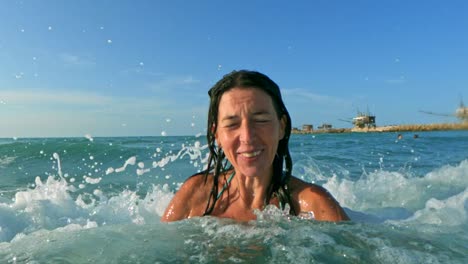 Beautiful-active-woman-having-fun-splashing-with-big-sea-waves-breaking-on-his-head