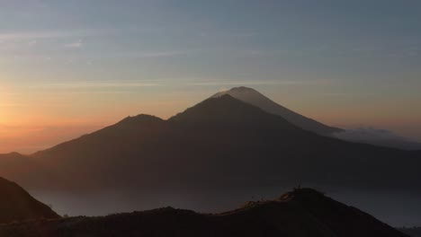 Tourist-standing-on-mount-Batur-ridge-during-magical-morning-sunrise-in-Bali,-aerial