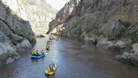 Aerial-view:-River-rafters-in-deep-canyon-pass-waterfall-on-the-right