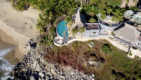 An-aerial-drone-panning-above-a-mansion-villa-on-a-paradise-beach-in-Sayulita,-Mexico