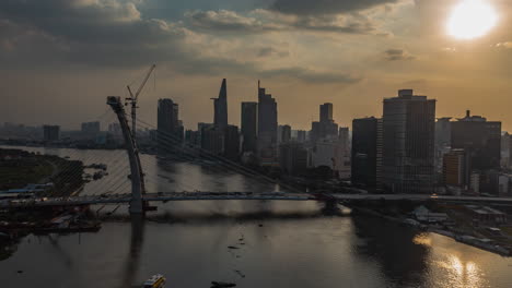 Classic-drone-hyperlapse-view-and-establishing-shot-of-Saigon-river,-Vietnam-from-drone-with-bridge-under-construction-view-and-modern-city-skyline-at-sunset