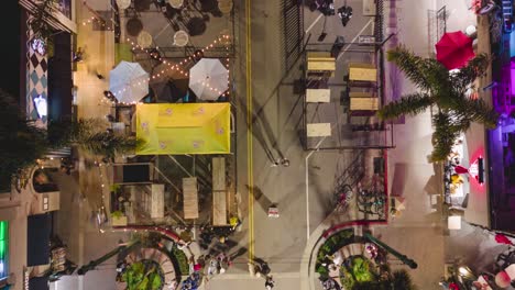 drone-time-lapse-of-main-street-in-Huntington-beach-at-night-with-bright-lights-and-colorful-crowds-with-bustling-street-filled-with-people-walking,-shopping,-and-dining