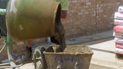 Bricklayer-Pours-Wet-Mortar-Into-A-Wheel-Barrow-From-A-Mixer,-SLOW-MOTION
