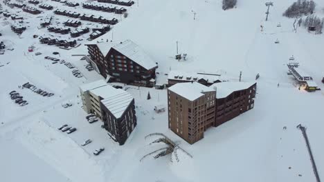 Myrkdalen-hotel-surrounded-by-apartment-buildings-and-ski-slopes-in-winter-morning---Aerial-looking-down-at-hotel-in-early-snowy-morning-with-skilift-in-background