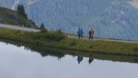 Group-Of-Hikers-Walking-Alongside-Lake-Pond-High-In-The-Alps-At-Dachstein-Austria