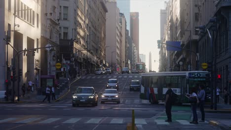 Peak-hour-traffics-on-the-road,-intersection-between-corrientes-and-leandro-n-alem-avenues,-with-pedestrians-walking-on-zebra-crossing,-buses-and-cars-driving-across-the-street-in-late-afternoon