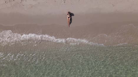 Vertical-aerial:-Young-Caucasian-woman-in-bikini-on-warm-sandy-beach