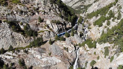 Aerial:-mountain-train-passing-by-a-beautiful-waterfall-in-the-Pyrenees