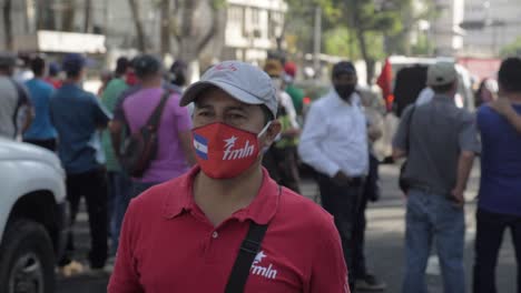 Man-walks-amidst-protesters-wearing-a-FMLN-face-mask-and-shirt---Slow-Motion