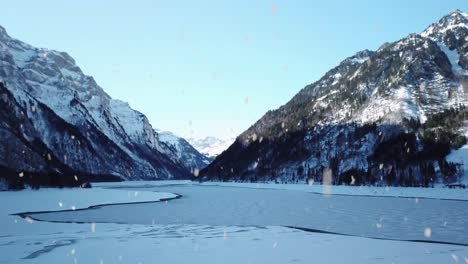 Agua-De-Lago-Congelada-Rodeada-De-Cordillera-Durante-Las-Nevadas,-Vista-Aérea-Lateral-Voladora
