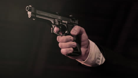 Close-up-on-man's-hands-in-suit-lifting-up-a-pistol,-dark-background