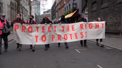 People-march-along-a-street-with-a-white-banner-with-orange-writing-on-that-reads,-“Protect-the-right-to-protest”-during-a-Kill-The-Bill-protest