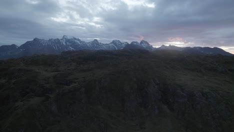 Aerial-view-over-a-mountain-revealing-the-dramatic-sunset-above-a-snowy-range---rising,-drone-shot