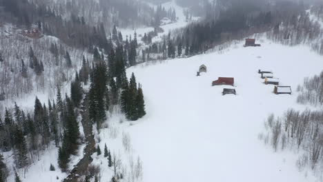 Small-buildings-covered-in-snow-in-mountain-landscape,-aerial-drone-view