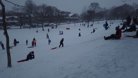 Wide-establishing-shot-of-kids-having-fun-on-a-crowded-community-tobogganing-hill-during-a-snowy-day