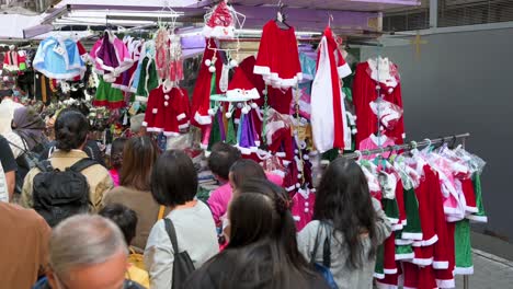 Pedestrians-walk-past-a-street-stall-selling-Christmas-merchandise-such-as-hats,-ornaments,-and-costumes-in-Hong-Kong