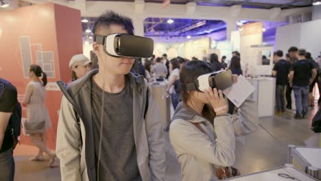 Asian-guy-wearing-360-virtual-reality-digital-headset-and-exploring-digital-world-at-technology-expo