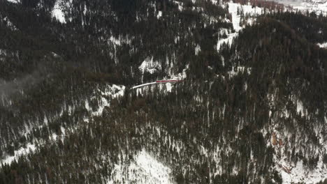 high-aerial-shot-over-forest-with-a-viaduct-in-the-center-while-a-red-train-is-passing-by