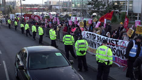 A-car-and-a-police-van-drive-past-people-holding-placards-and-banners-on-a-Stand-Up-To-Racism-anti-fascist-protest