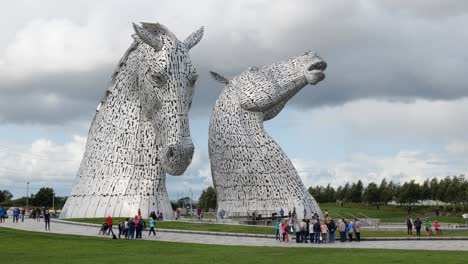 Artistic-statue-The-Kelpies,-metal-horses-heads-in-Falkirk,-Scotland-created-by-Andy-Scott-with-tourist-visiting-the-landmark