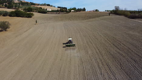 Tractor-plowing-ground-soil-in-rural-agriculture-wheat-field-aerial-view-in-Pienza,-Tuscany