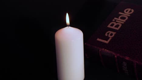 White-holy-candle-flame-burning-next-to-bible-against-black-background